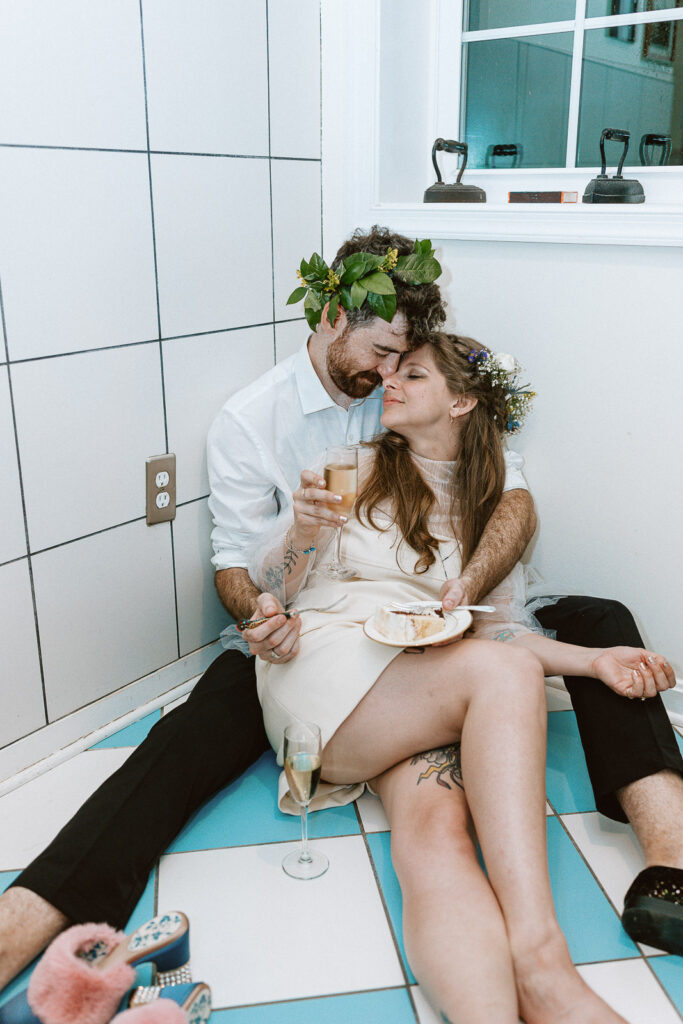 An unconventional and joyous image depicting the non-traditional portraits captured during the cake and champagne celebration in the laundry room, with blue and white tiles providing a unique canvas for iconic moments reflecting their love.