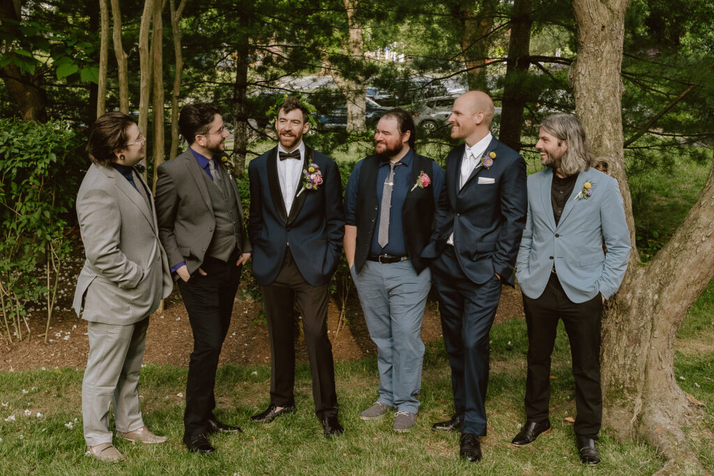 An image highlighting the distinctive wedding attire of the groom and his groomsmen. From the groom's Virgo pin in honor of the bride's astrology sign to the varied styles of the groomsmen, the photo captures the essence of their unique and fashionable choices for the iconic Virginia backyard celebration.