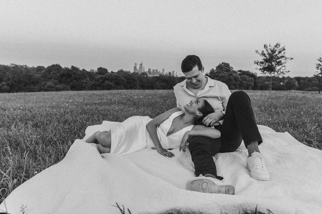couple laying on a blanket at belmont plateau for their engagement photos in philadelphia