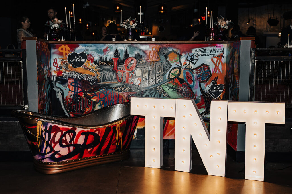inside of Spin in Philadelphia at a wedding, showing a tub with graffiti, neon lights that say "TNT" and showing the bar