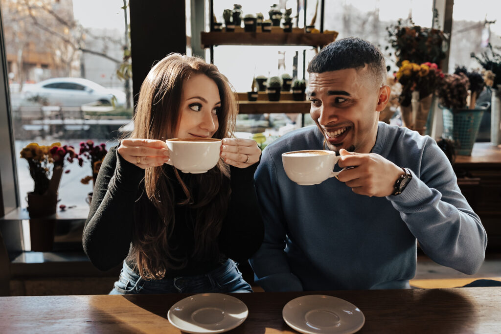 Couple enjoying a coffee date during their engagement session in Washington DC, sharing smiles and warm mugs in a cozy café setting.