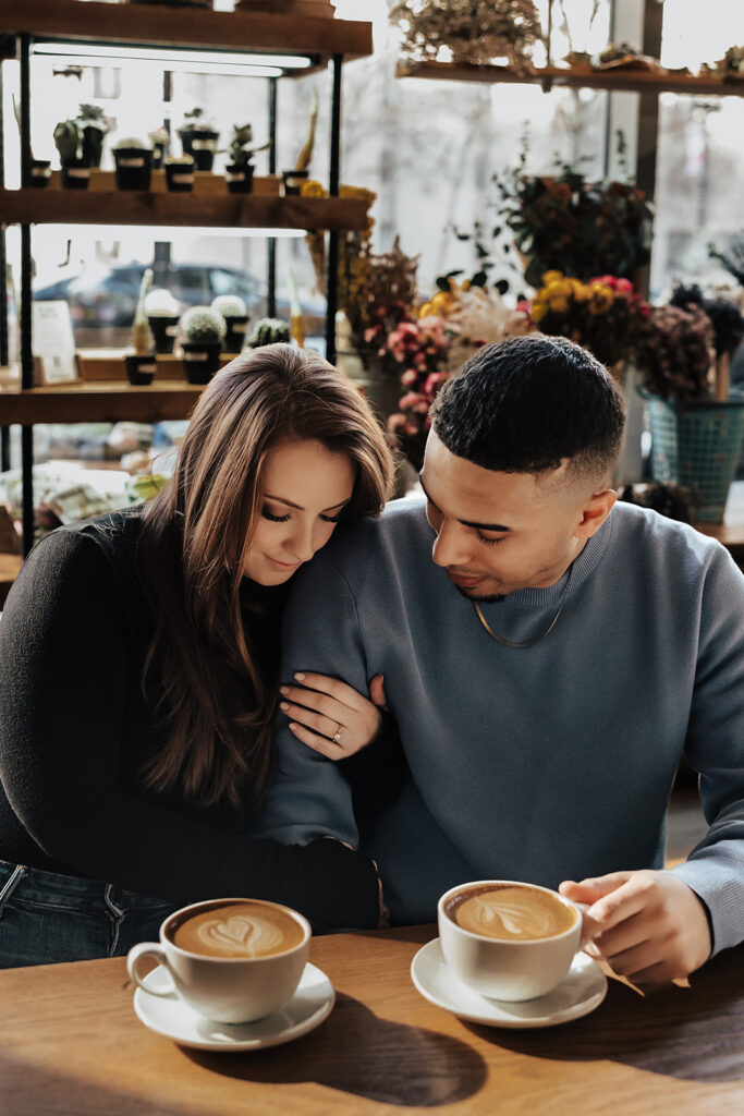 Couple enjoying a coffee date during their engagement session in Washington DC, sharing smiles and warm mugs in a cozy café setting.